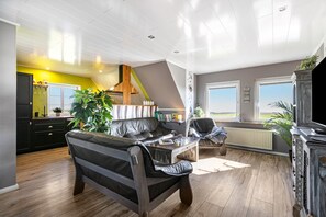 Een moderne woonkamer met een bank, salontafel en open haard. Een trap leidt naar een hoger niveau, en grote ramen zorgen voor natuurlijk licht.