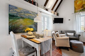 A dining area with a table, chairs, a painting, and a television on the wall. - Holiday Apartment 'Hyggelig Am Deich - Ockholm' with Private Terrace, Shared Garden & Wi-Fi (Ockholm)