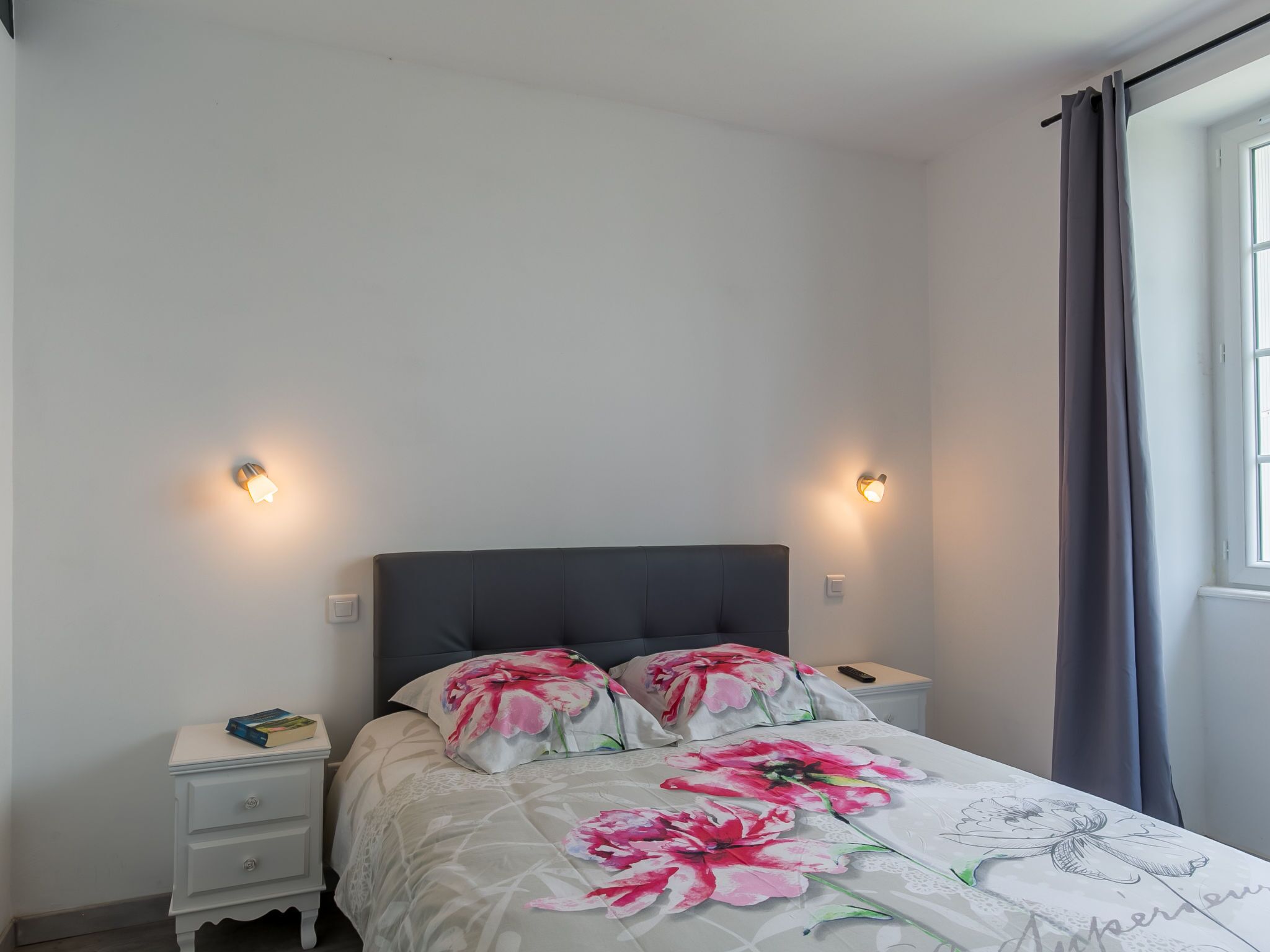 A bedroom with a bed, two bedside tables, and a window with curtains.