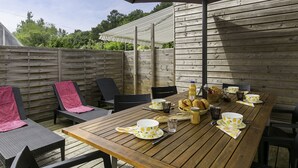 Una terraza de madera al aire libre con una mesa dispuesta para el desayuno, incluyendo cruasanes, tazas de café y una botella de jugo.