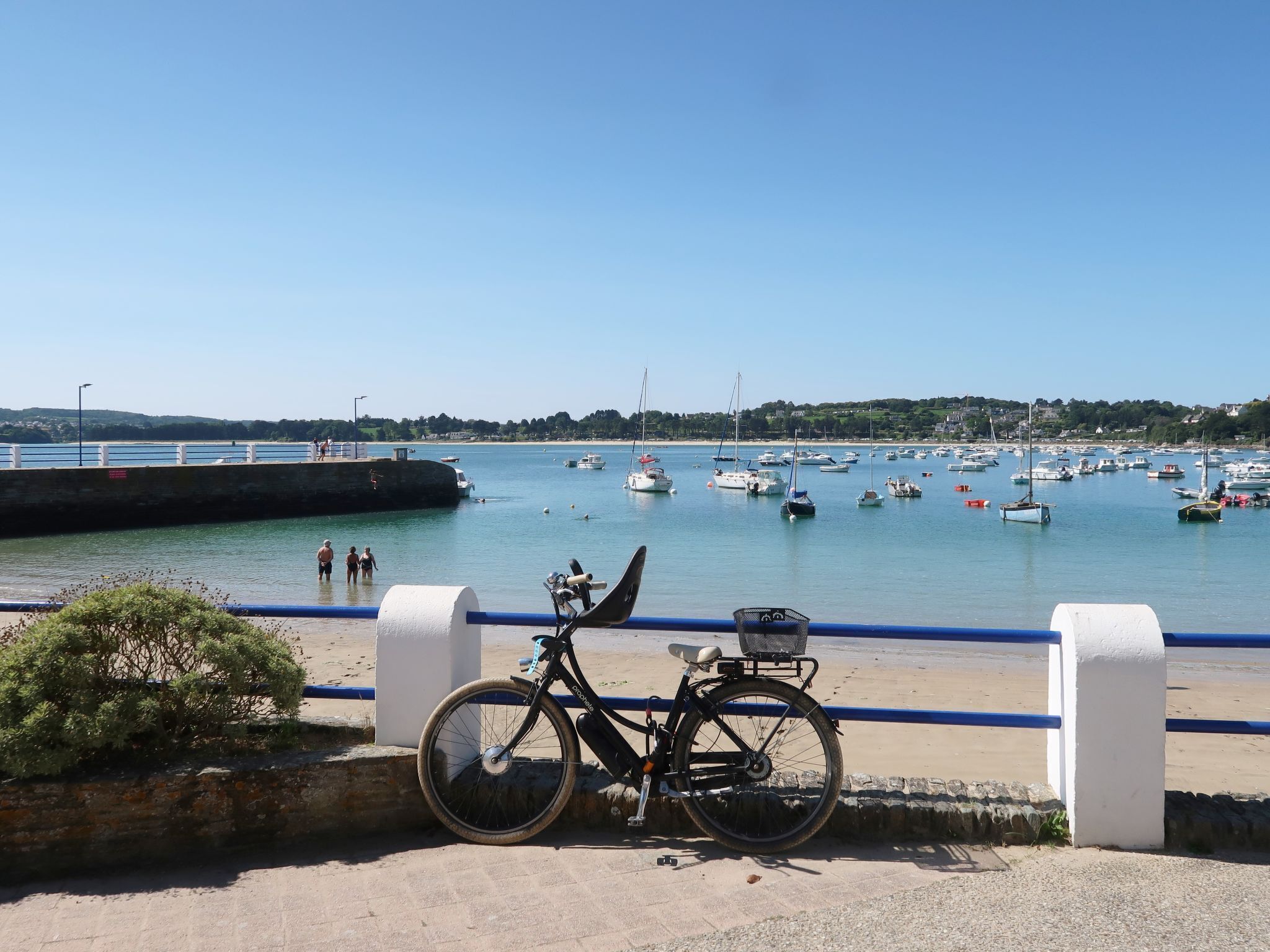 A bicycle parked by a waterfront with a clear view of boats and a distant shoreline.