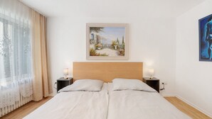 A double bed with a wooden headboard, two bedside tables with lamps, a window with sheer curtains, and a framed painting above the bed. - Apartment 'Haus Annenberg' with Shared Terrace, Shared Garden and Wi-Fi (Monzelfeld)