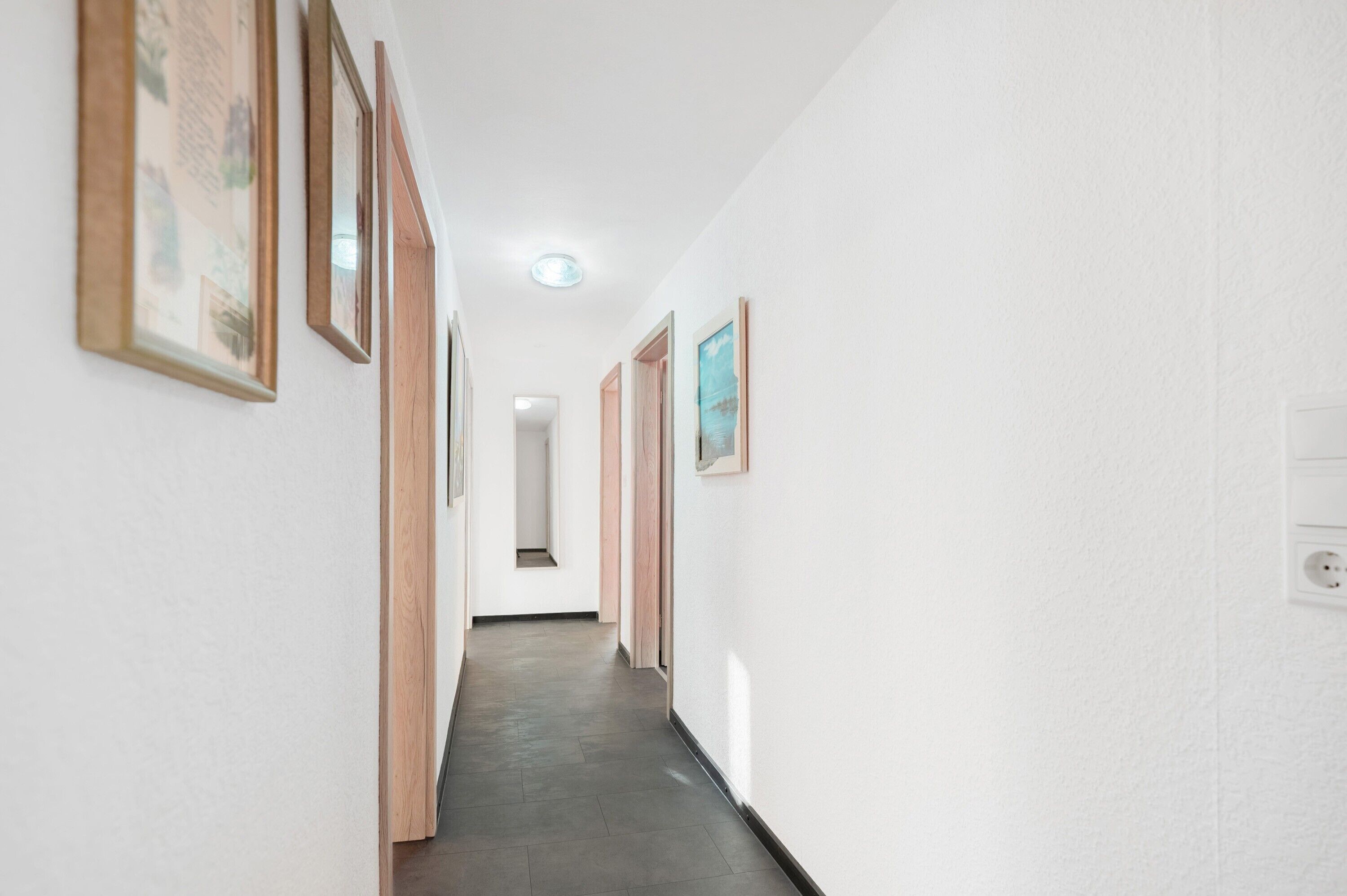 A hallway with framed pictures on the walls, a light switch, and a door at the end.