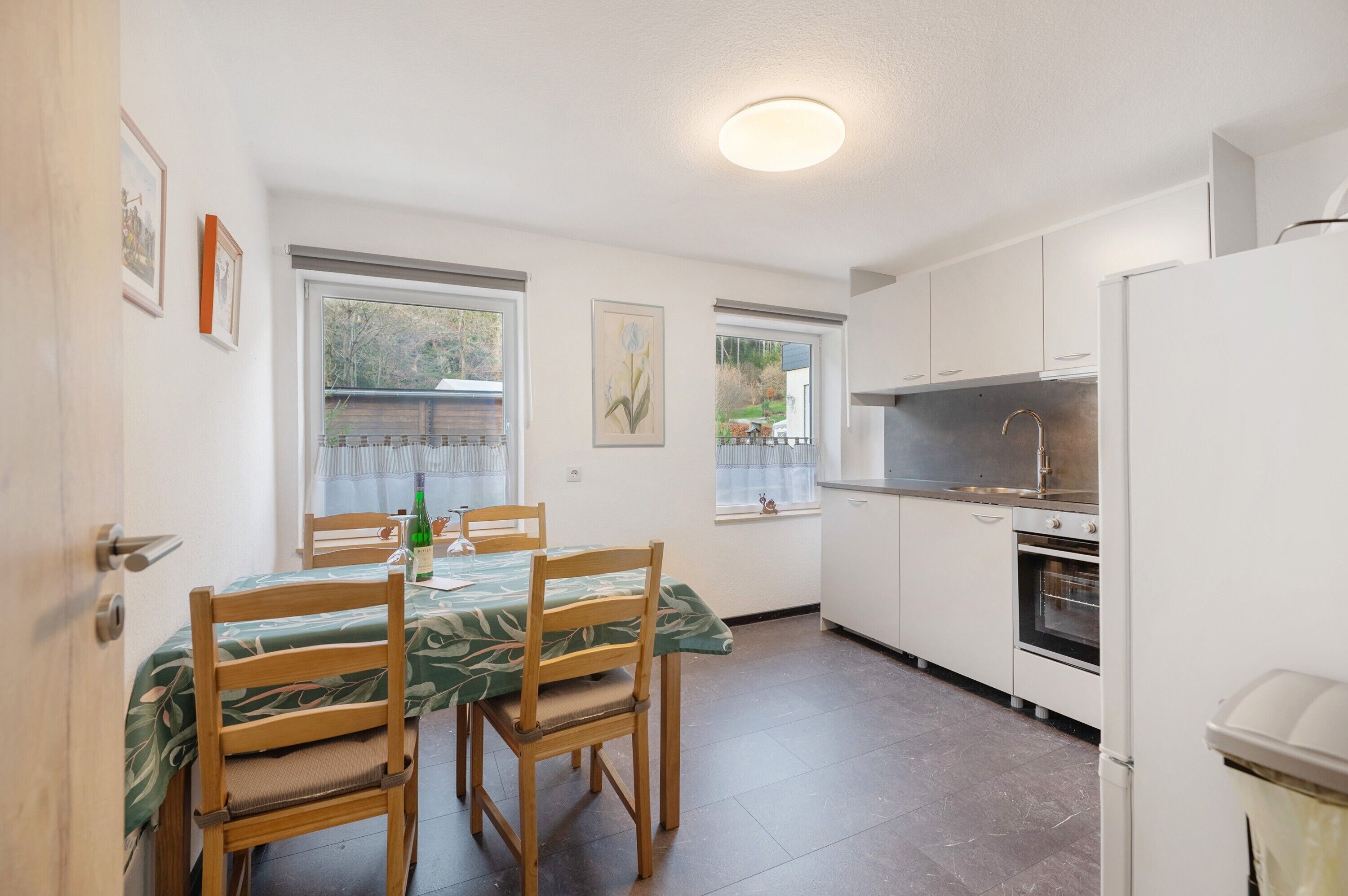 A compact kitchen with white cabinets, a built-in oven, and a dining area with a table and chairs.
