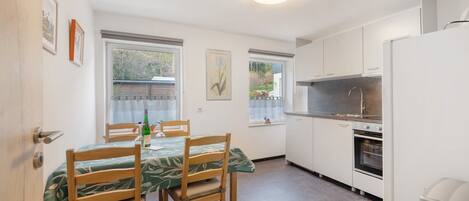 A compact kitchen with white cabinets, a built-in oven, and a dining area with a table and chairs.