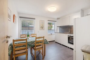 A compact kitchen with white cabinets, a built-in oven, and a dining area with a table and chairs. - Apartment 'Haus Annenberg' with Shared Terrace, Shared Garden and Wi-Fi (Monzelfeld)