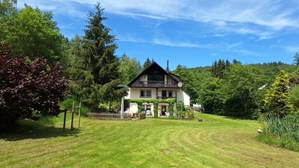 A house with a sloped roof, surrounded by a well-maintained lawn and trees. - Apartment 'Haus Annenberg' with Shared Terrace, Shared Garden and Wi-Fi (Monzelfeld)