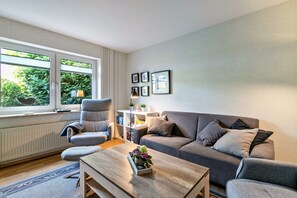 Una sala de estar moderna con un sofá gris, una mesa de centro de madera, un sillón gris y una ventana con persianas.