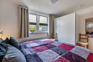 A bedroom with a bed, a window, a chair, and a radiator.