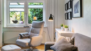 Un salon moderne avec un fauteuil gris, un canapé, une lampe sur pied et une fenêtre donnant sur un paysage verdoyant.