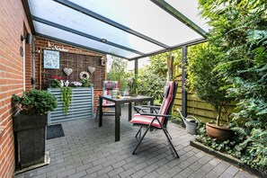 A patio with a table and chairs, a brick wall, a pergola, and potted plants.