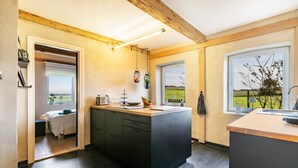 Een moderne keuken met een centraal eiland, houten balken en grote ramen met uitzicht op het platteland.