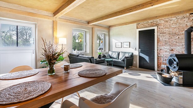 Een moderne woonkamer met een houten eettafel, witte stoelen, een open haard en een bakstenen muur.