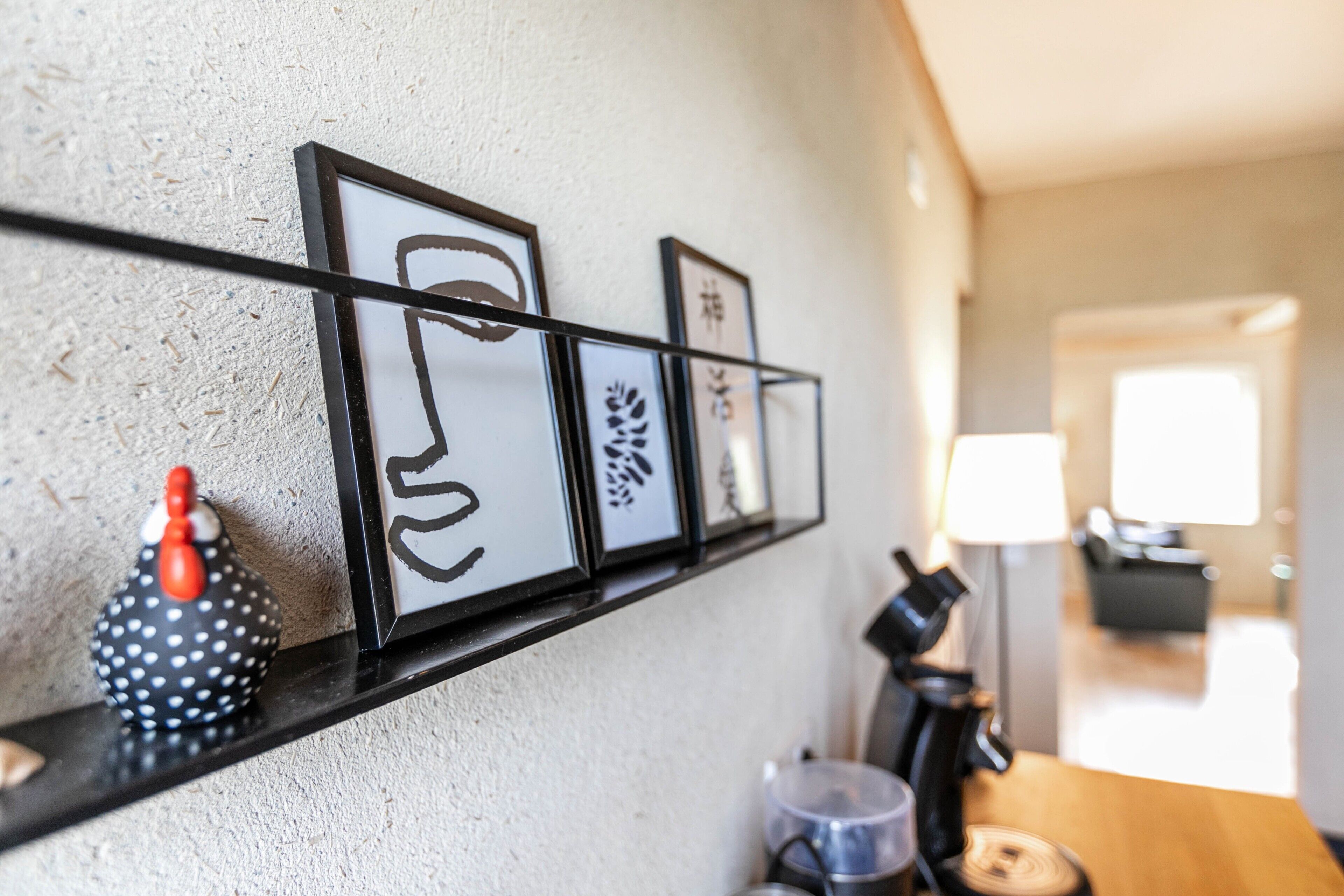 A kitchen with a coffee machine, a kettle, and a shelf with framed artwork.