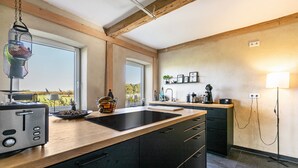 Een moderne keuken met een houten aanrecht, zwarte kastjes, een zwart inductiekookveld en een hangende vogelvoeder.