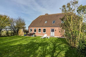 Een huis van baksteen met een schuin dak, een gazon, een witte lounge stoel en een klein terras.