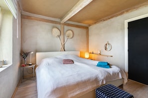 Een slaapkamer met een bed, nachtkastje, lamp, wanddecoratie en een deur.