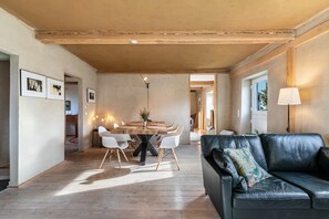 Een ruime woonkamer met een eettafel, een zwarte leren bank en een lamp.