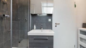 A modern bathroom with a glass shower enclosure, a white sink with a mirror above, and a built-in cabinet with drawers.
