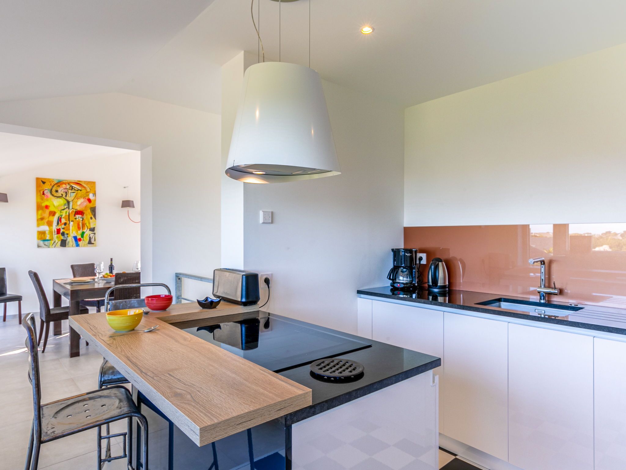 Una cocina moderna con una isla central, un comedor con sillas y una estación de café.