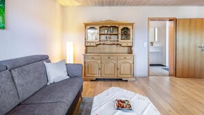 A living room with a grey sofa, a wooden cabinet with glass doors, and a door leading to another room. - Triberg-Blick Apartment with Mountain View, Terrace and Wi-Fi (Triberg im Schwarzwald)