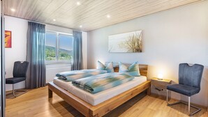 A bedroom with a wooden bed, a nightstand, a chair, a window with curtains, and a painting on the wall. - Triberg-Blick Apartment with Mountain View, Terrace and Wi-Fi (Triberg im Schwarzwald)
