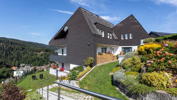 A two-story house with a sloped roof, a balcony with potted plants, and a well-maintained lawn. - Triberg-Blick Apartment with Mountain View, Terrace and Wi-Fi (Triberg im Schwarzwald)
