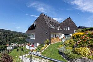 A two-story house with a sloped roof, a balcony with potted plants, and a well-maintained lawn.