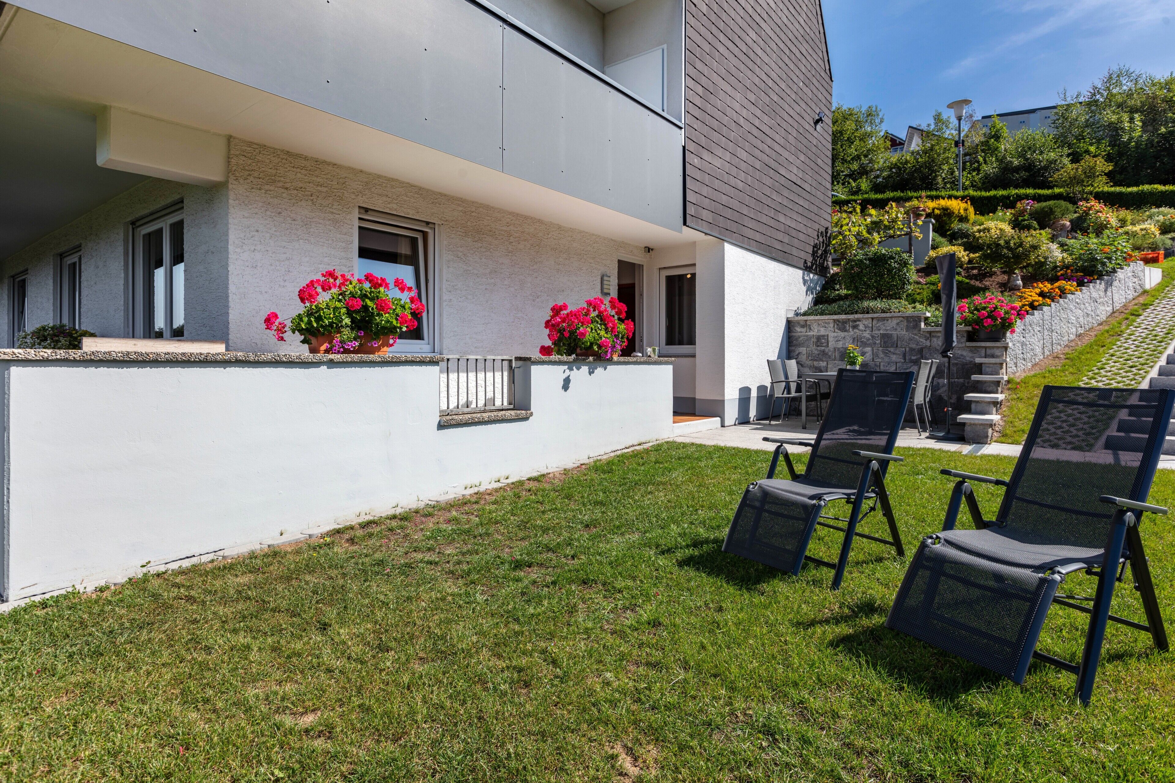 A modern building with a balcony, outdoor seating, and a well-maintained garden.