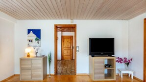 Ein Wohnzimmer mit Holzboden, einem Fernsehschrank, einer Lampe, einem Gemälde und einer Tür zu einem anderen Raum.
