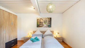Ein Schlafzimmer mit einem hölzernen Kleiderschrank, einem Bett mit weißer Bettwäsche, einem Bild einer Tür und Nachttischlampen.