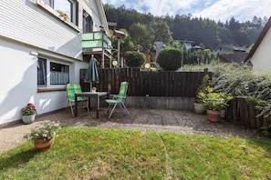 A patio area with a table and chairs, a wooden fence, and potted plants.