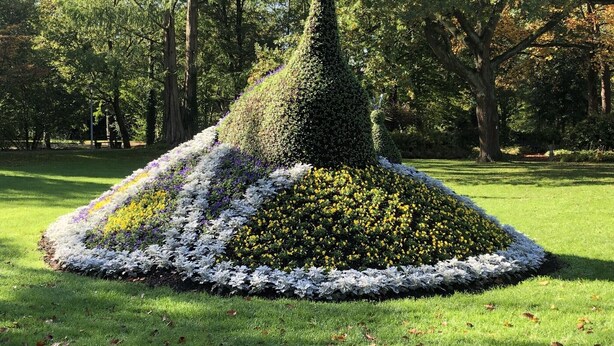 Ein Formschnittgarten mit einer kegelförmigen Baumskulptur, umgeben von Blumenbeeten.