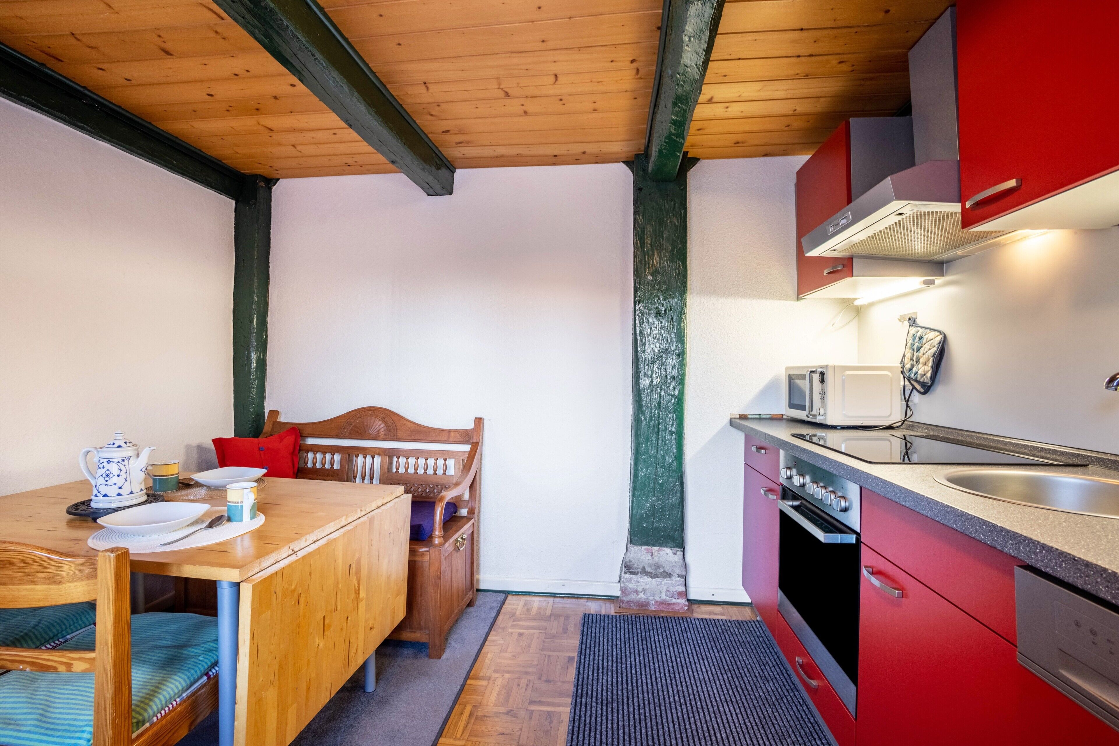 A compact kitchen with a wooden table, red cabinets, a microwave, and a built-in oven.
