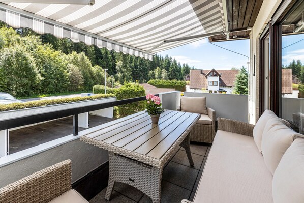 A balcony with a table, wicker furniture, and a view of a residential area.