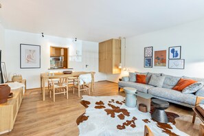 A modern living room with a sofa, a dining table, and a kitchen area in the background.