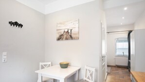 Ein Essbereich mit einem weißen Tisch und Stühlen, einer Schüssel auf dem Tisch, einem Gemälde an der Wand und Blick auf das Meer durch ein Fenster.