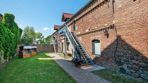 A brick building with a staircase leading to an upper level, a covered outdoor area, and a paved walkway. - Studio Apartment 'Appartement 2 - Galopp' with Shared Terrace and Wi-Fi (Ludwigsfelde)