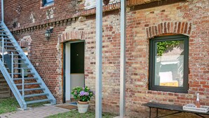 A brick building with a metal staircase, a door, a window, and a small table with a potted plant. - Studio Apartment 'Appartement 2 - Galopp' with Shared Terrace and Wi-Fi (Ludwigsfelde)