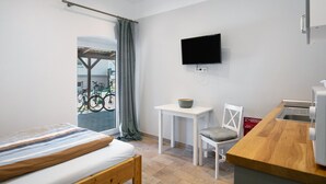 A modern room with a bed, a small table, a chair, a TV, and a kitchenette. - Studio Apartment 'Appartement 2 - Galopp' with Shared Terrace and Wi-Fi (Ludwigsfelde)