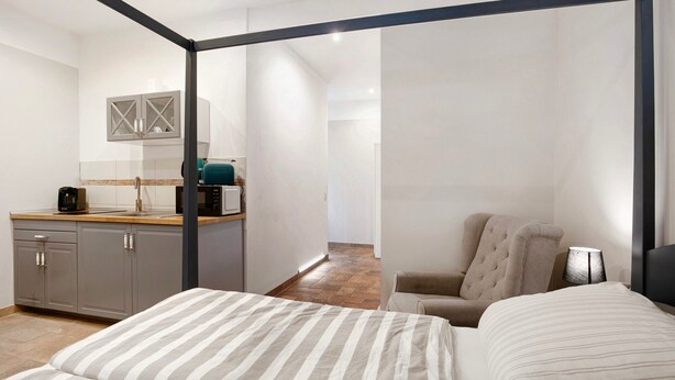 Una habitación de hotel moderna con cama, una silla, un escritorio con computadora y una zona de cocina.