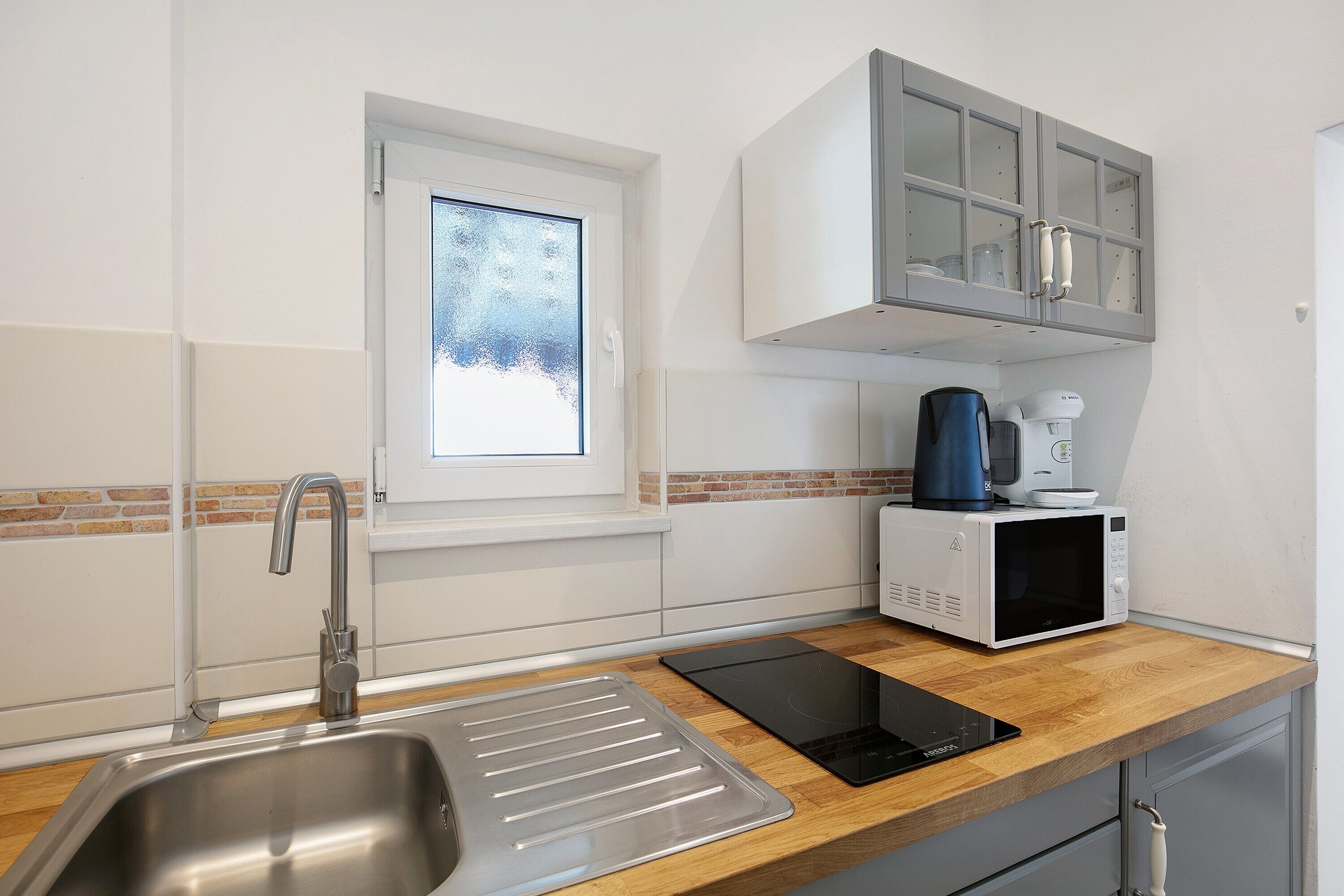 A modern kitchen with a stainless steel sink, a window, a microwave, and a built-in oven.