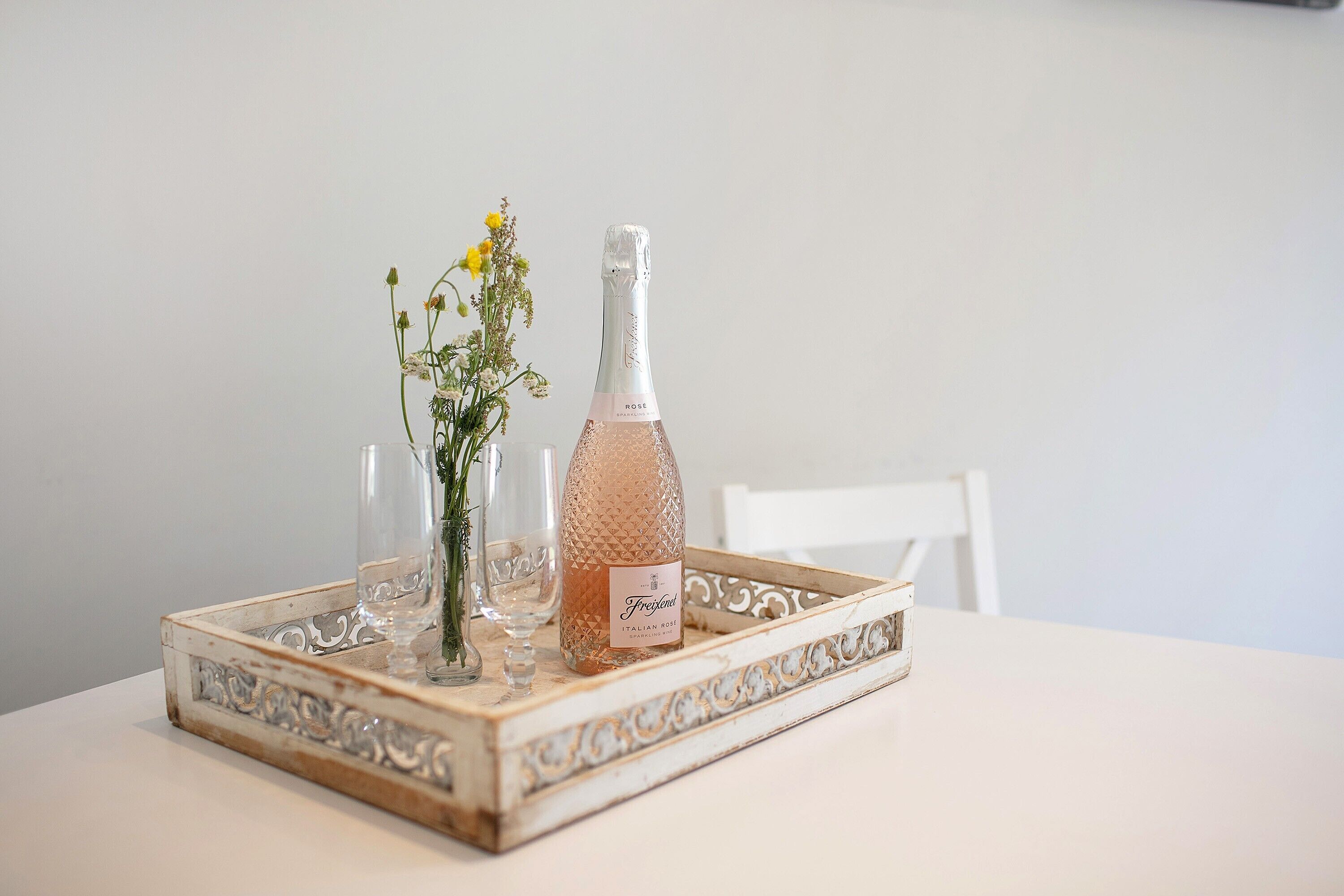 Een tafel met een champagnefles, een glas en een bloemenvaas op een decoratief dienblad.