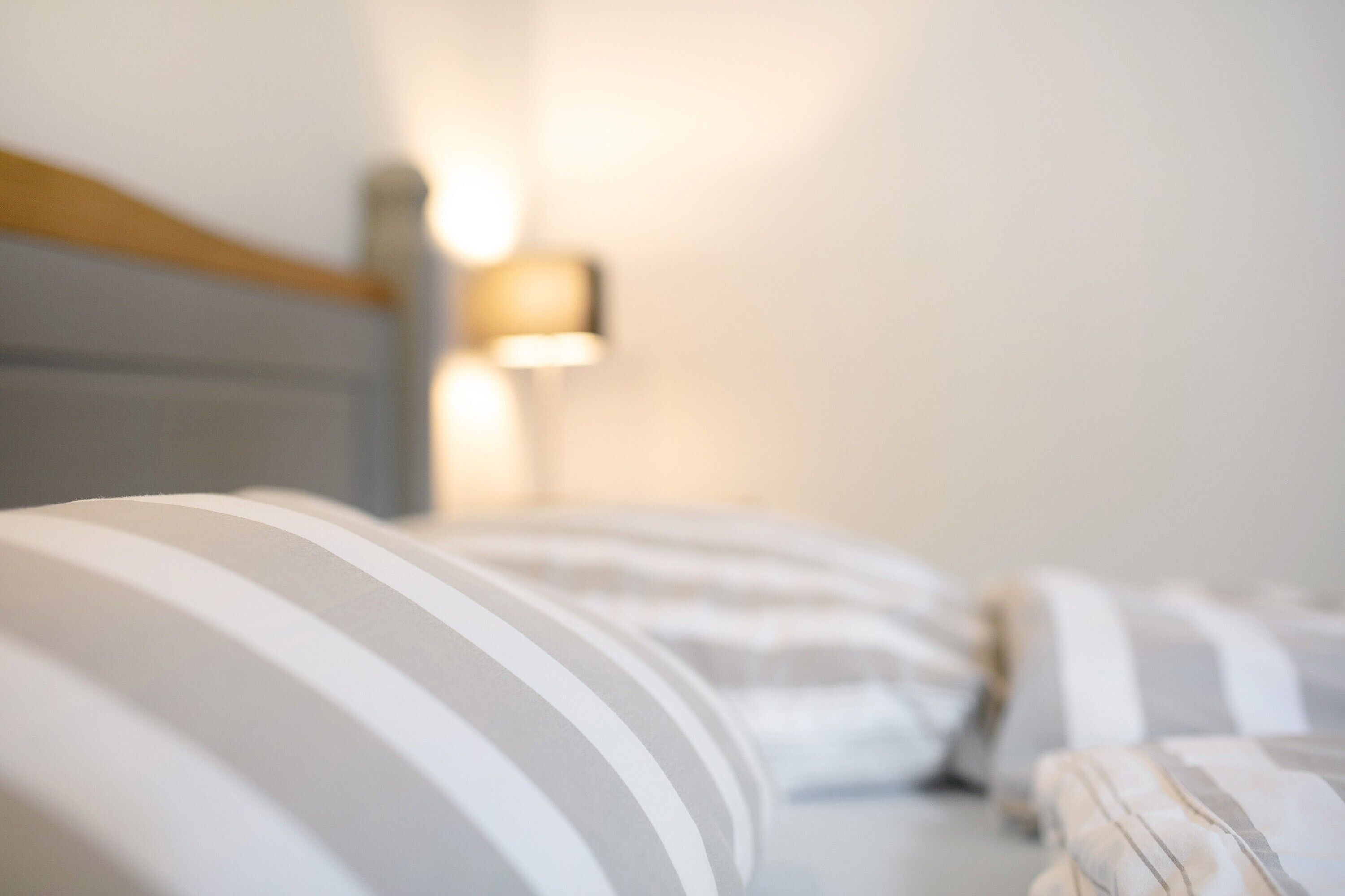 A bed with striped bedding and a wall-mounted lamp.