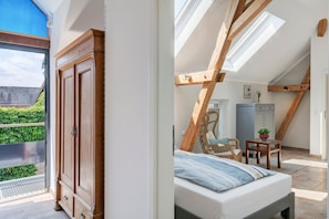 A bedroom with a skylight, a bed, a wardrobe, a chair, and a small table.
