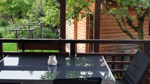 Una mesa con cubierta de vidrio, un jarrón blanco, una terraza de madera y una valla de madera.