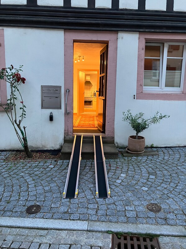 Une entrée d’immeuble avec un escalier menant à une porte, un pot de fleurs et une boîte de raccordement au sol.
