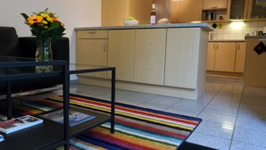 Una cocina moderna con armarios de madera, una encimera y una zona de comedor con una mesa negra y una alfombra colorida a rayas.