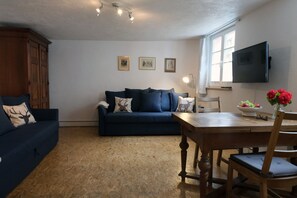 A living room with a dark blue sofa, wooden dining table, and a television mounted on the wall.