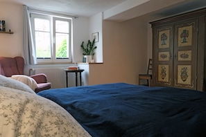 A bedroom with a large bed, a chair, a radiator, a window, and a cabinet with framed pictures.